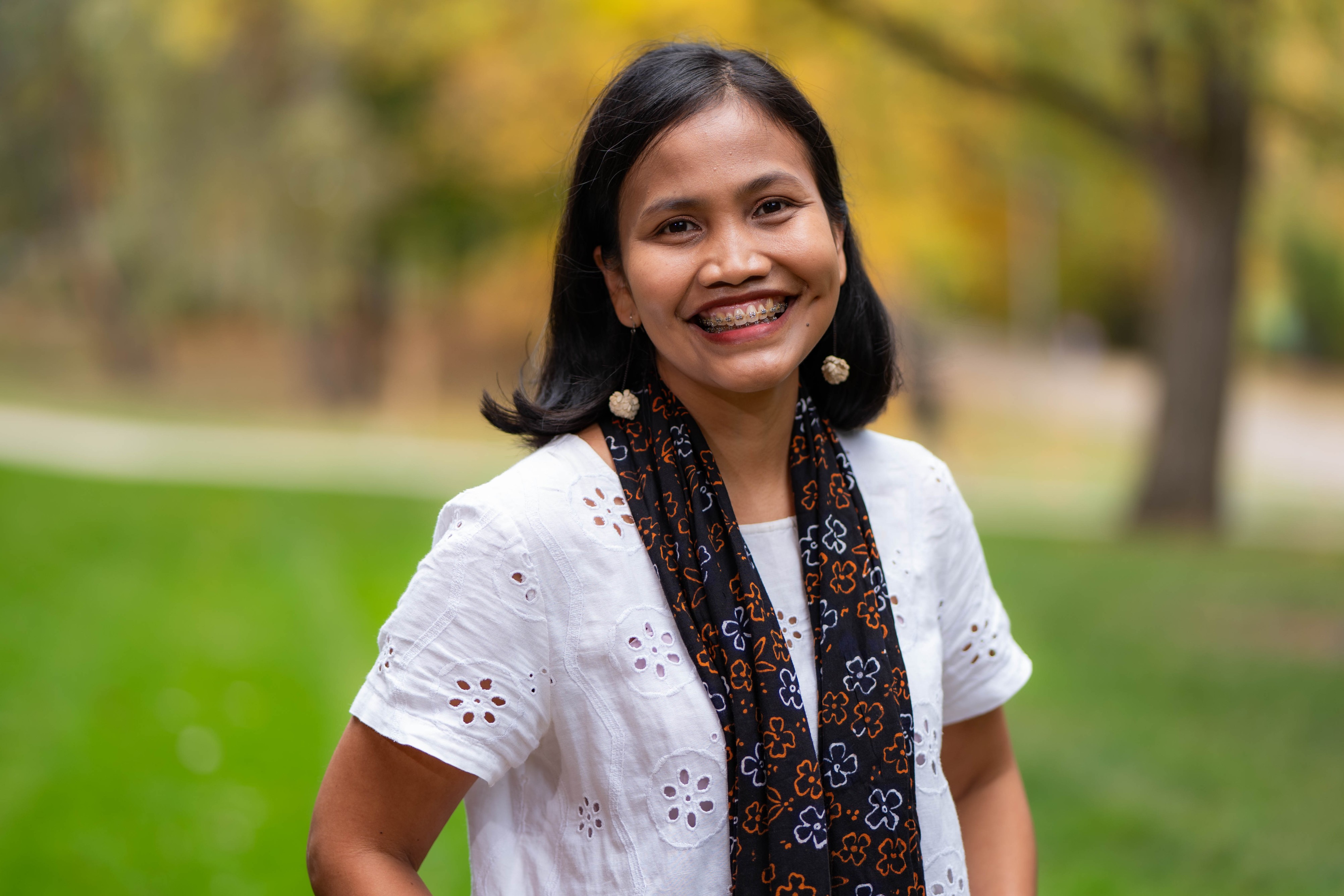 Prawita standing outside, wearing a white shirt and a black scarf.