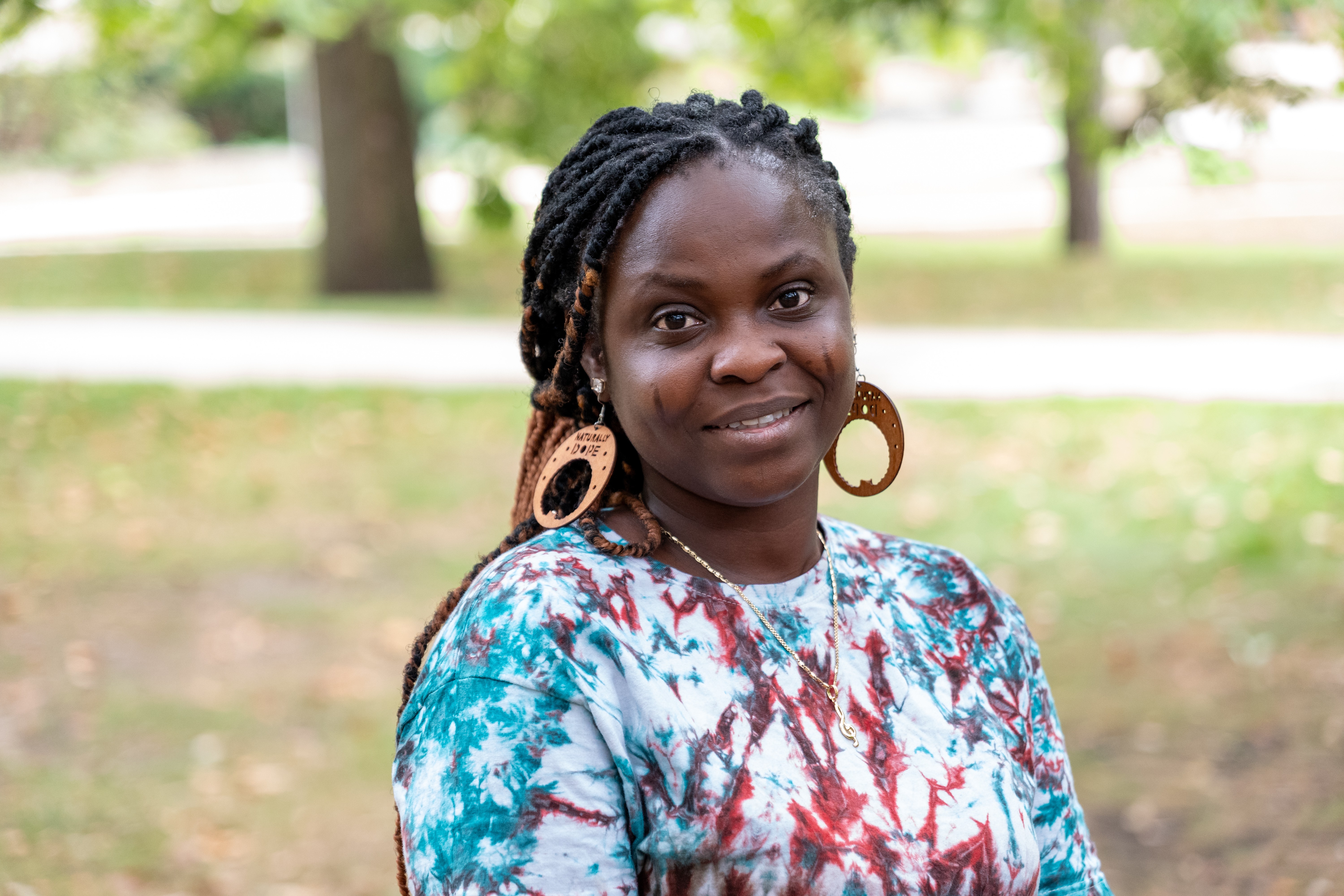 Yetunde in a red, white, and blue tie dye shirt, standing outside.