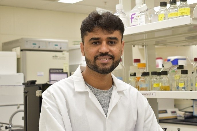 Azam seated in a laboratory and wearing a white lab coat.