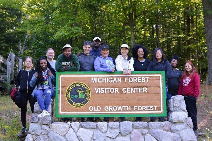 Nathan Moore amongst a group of people, standing behind a sign that reads, "Michigan Forest Visitor Center, Old Growth Forest."