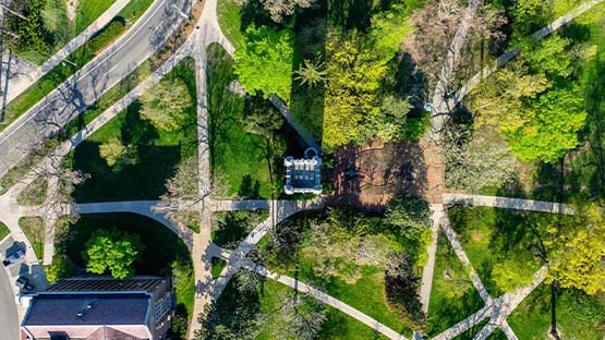 A drone photo taken from above Beaumont Tower. A crisscross of sidewalks can be seen among the bright green grass and trees.