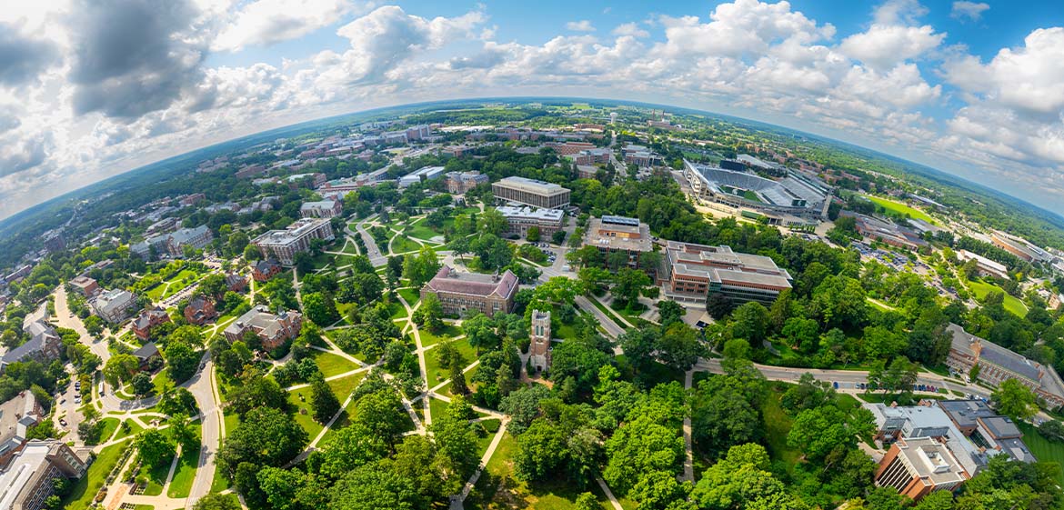 A drone photo of campus shows campus buildings dotted along vast green spaces up to a curved horizon.