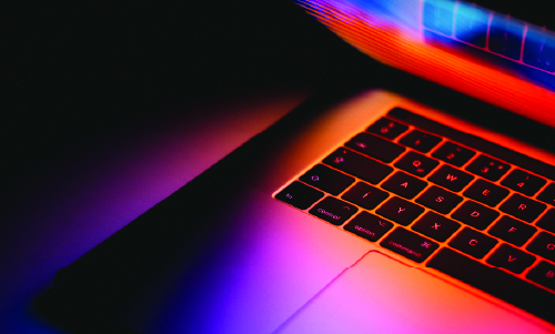 A laptop, partially closed, with a pink hued screen glow cast on the keyboard