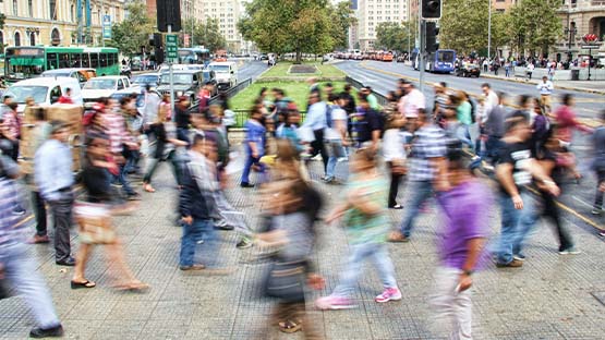 A photo of a crowd crossing the street with the movement causing the people to blur while cars and buildings in the background are clearly visible