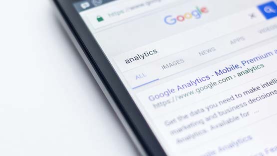 A phone screen displays Google search results for the term "analytics" with Google Analytics as the top result