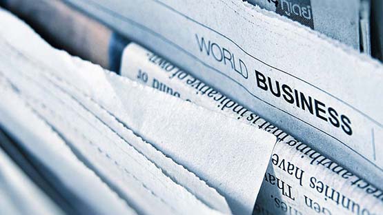 A photo of a stack of newspaper page edges. A section headline reading "World Business" is visible.