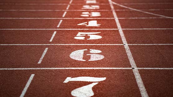 The lane numbers on a brownish red colored running track appear stacked vertically