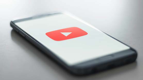 A black iPhone sits on a table with a YouTube logo on a white background displayed on the screen.