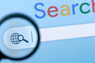 A photo of a Google search browser. A magnifying glass is held over the search icon.