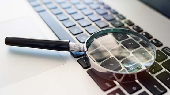 A magnifying glass sits on top of a silver and black MacBook keyboard.