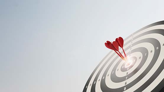 A photo of a black and white archery target with three red darts hitting the bullseye