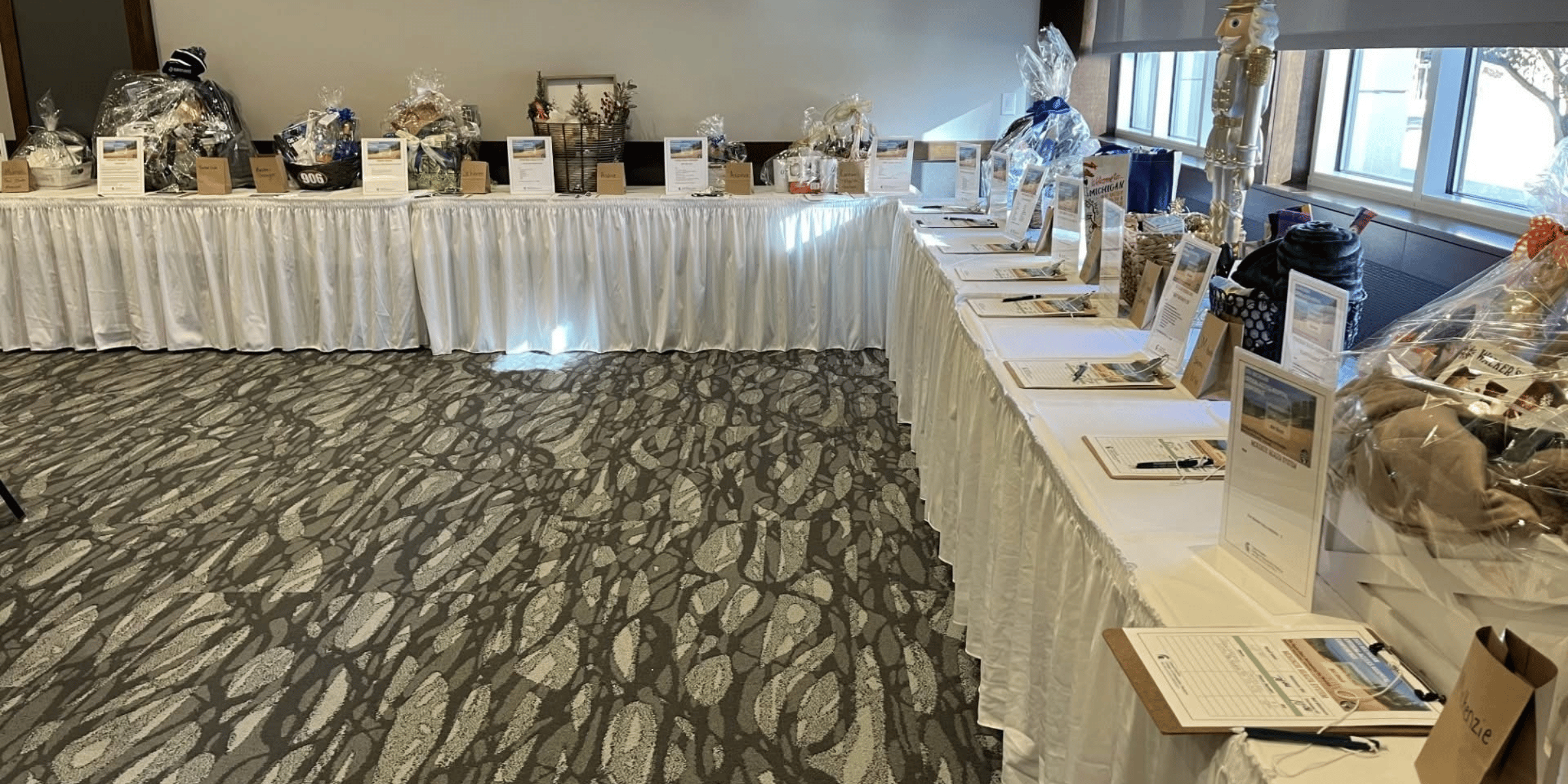 A table with white tablecloth displaying gift baskets wrapped in clear plastic with descriptions and clipboards.