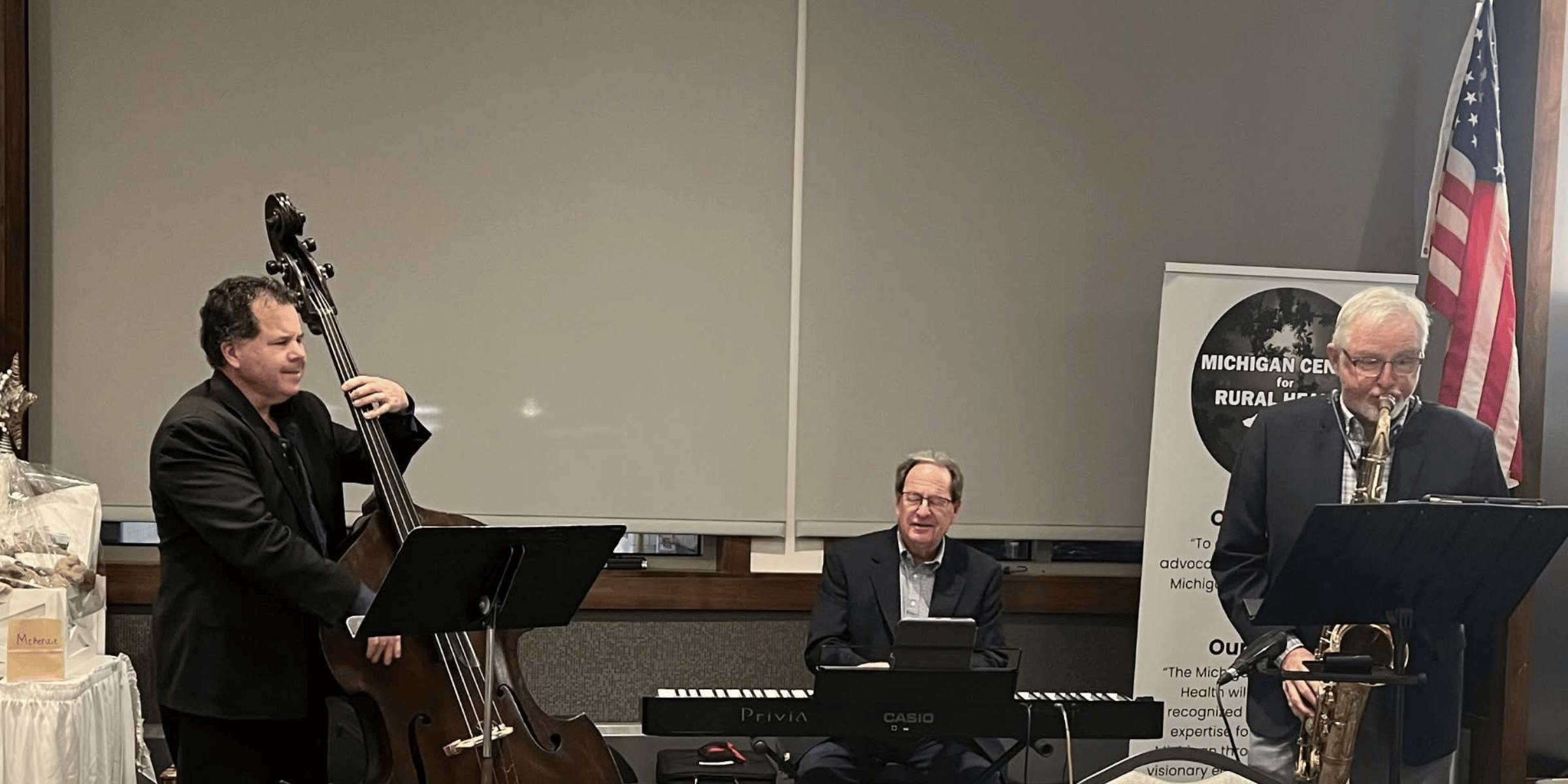 Three musicians performing indoors: a bassist, a keyboardist, and a saxophonist.