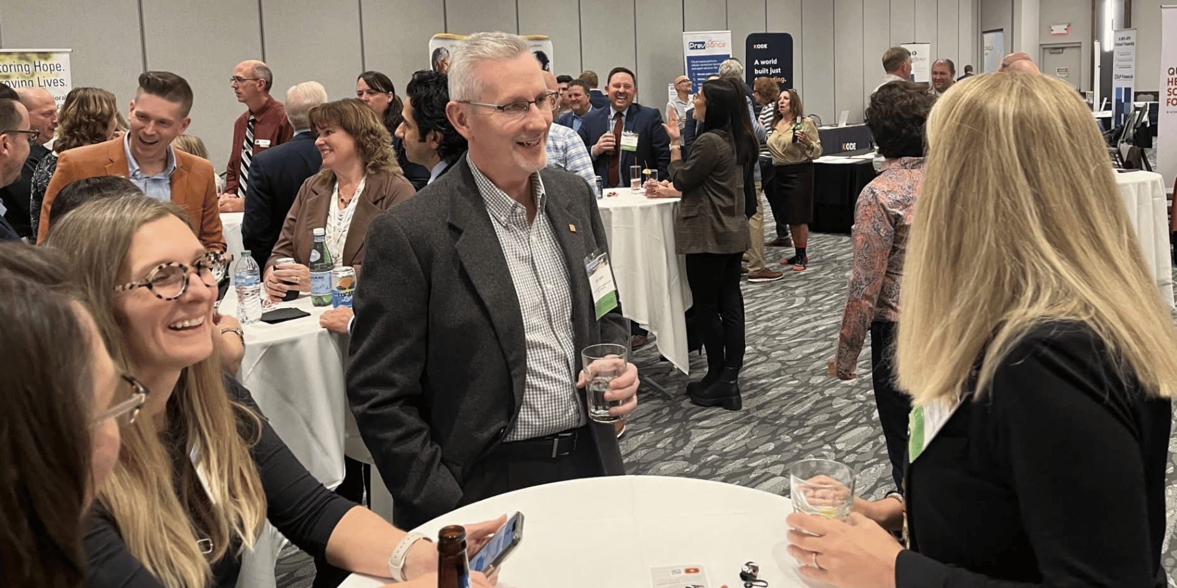 People mingling at a professional networking event with informational booths in the background.