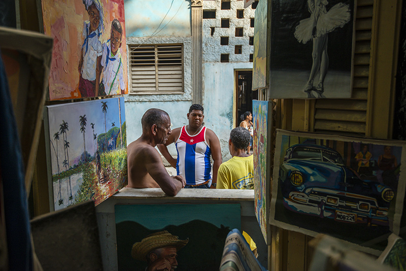 Three men talk outside a window decorated with paintings