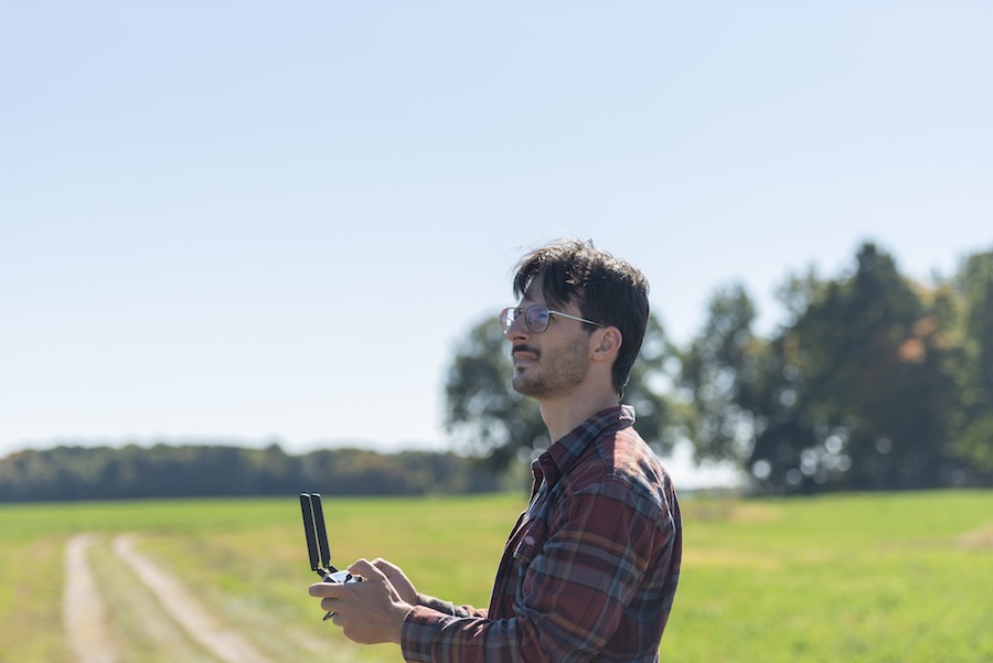 Leo Baldiga flies a drone with a remote control while standing in a farm field