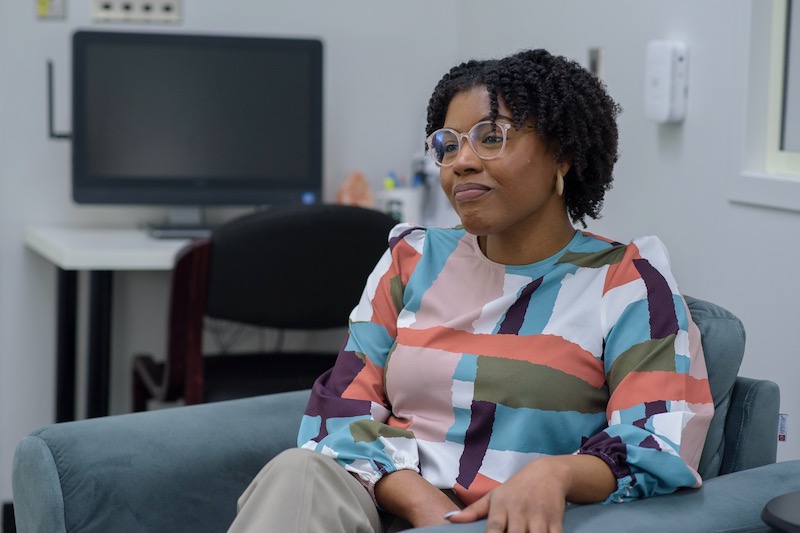 Deja Young is a doctoral candidate and previous therapist at the clinic. She is seating in a blue chair.