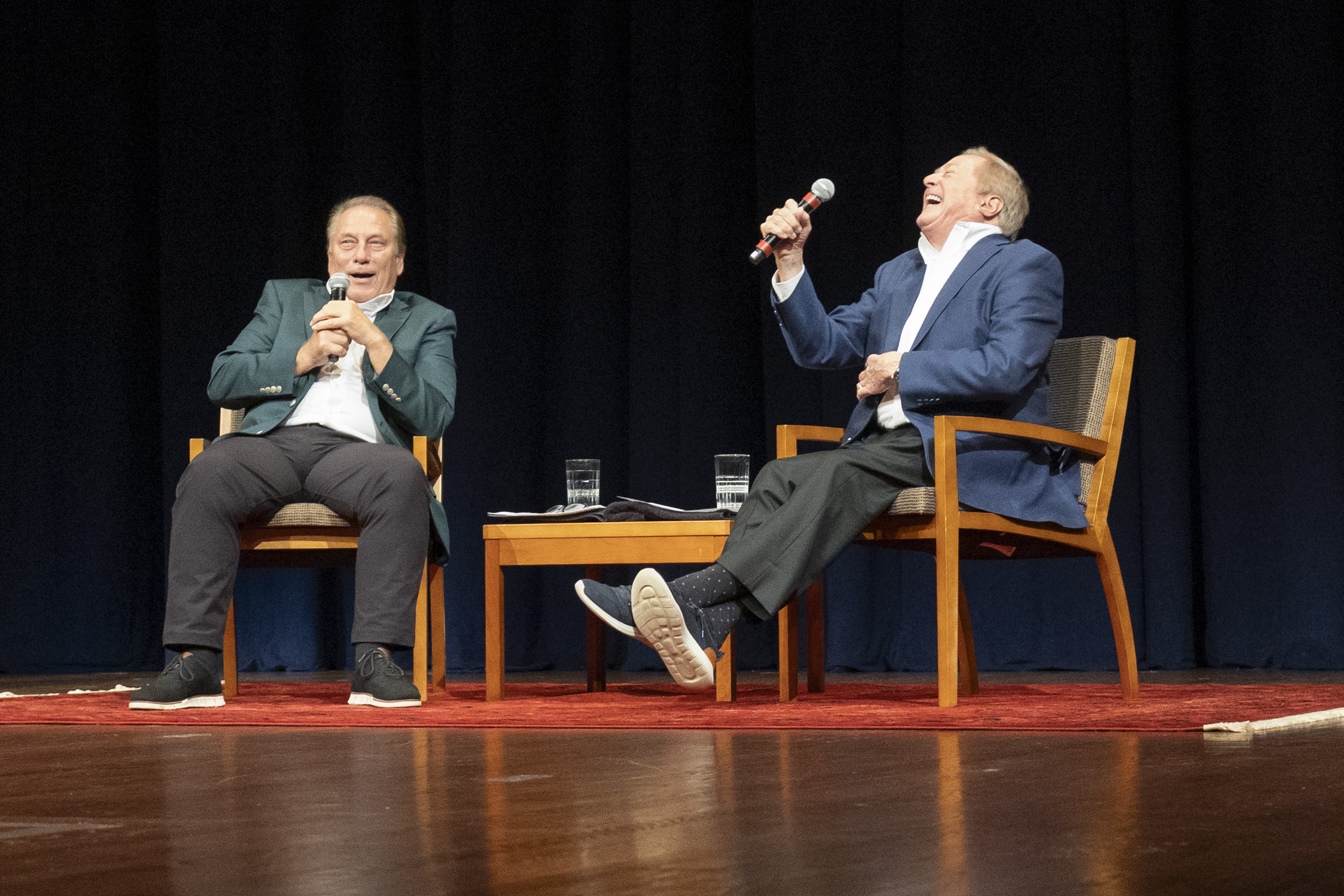 Coach Tom Izzo and Governor Jim Blanchard Sitting in chairs on the Pasant Theater stage holding microphones and laughing