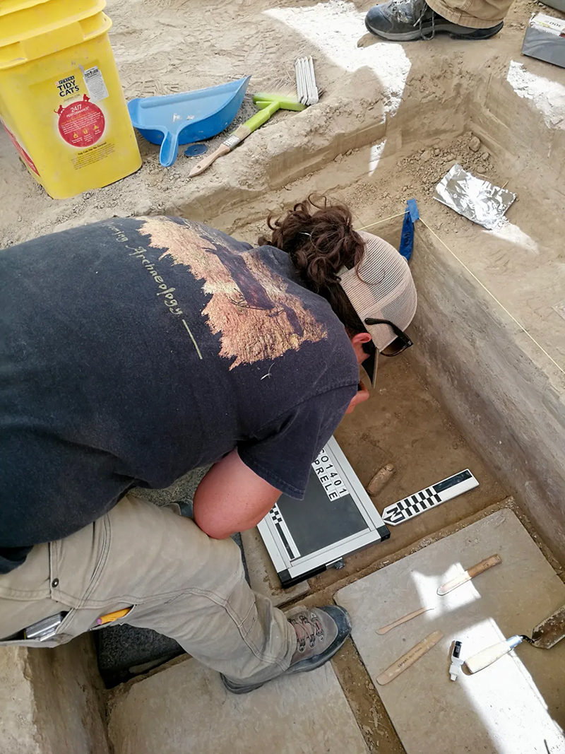 A woman works in dirt at an archaeology dig site