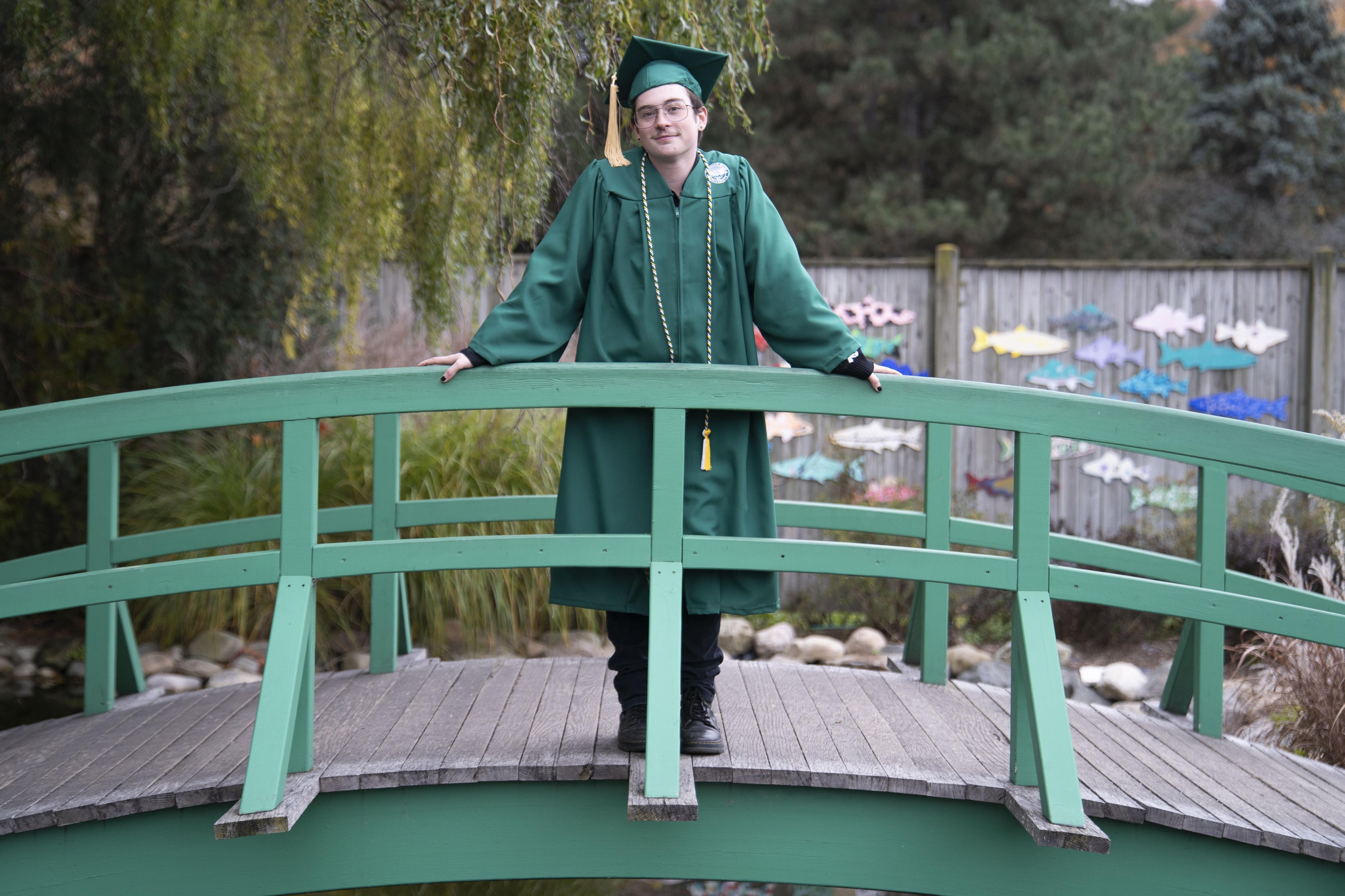 Onyx Bromley stands on a bridge in a MSU cap and gown
