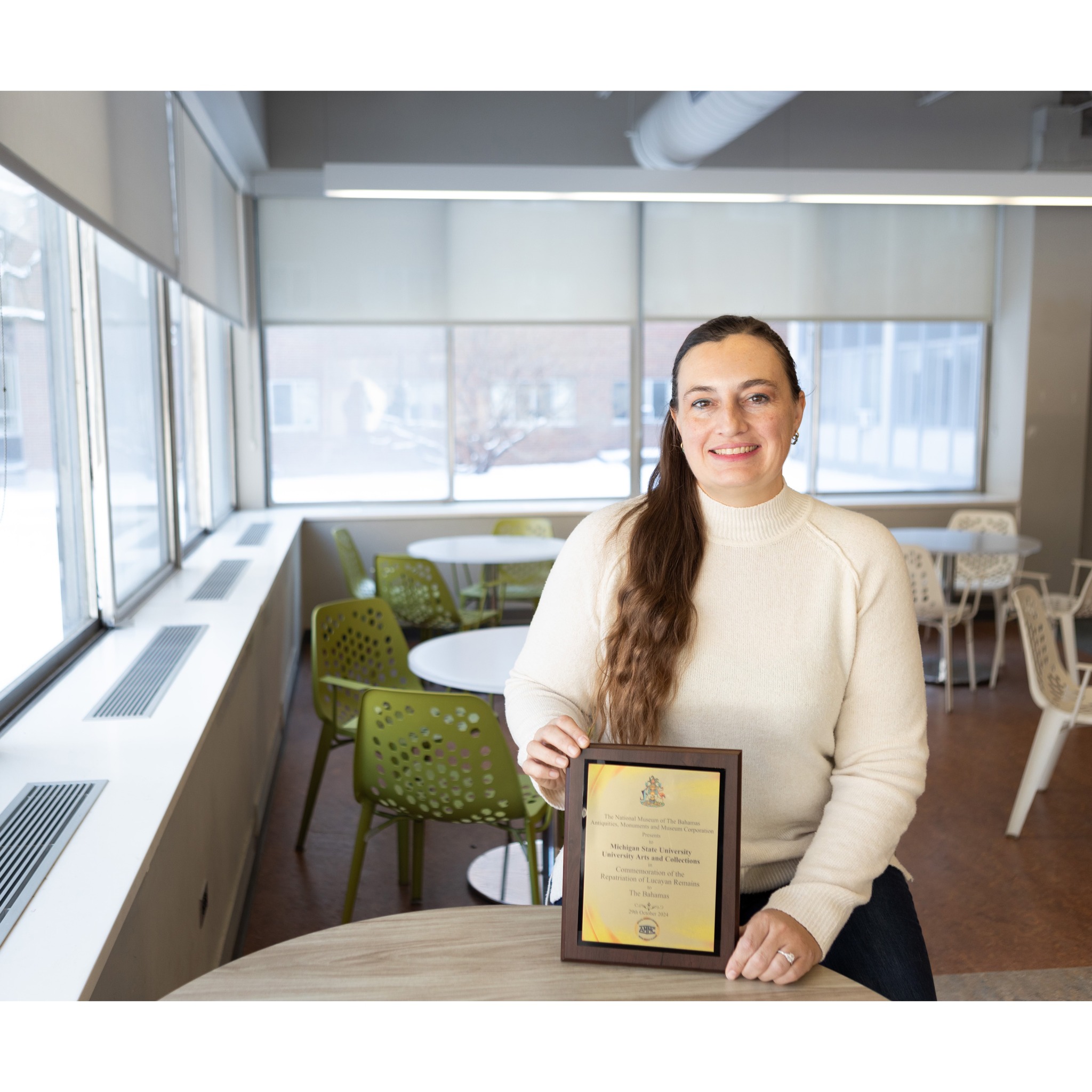Jessica Yann holds a plaque while sitting at a table
