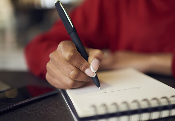 Person's hands, writing on a notepad