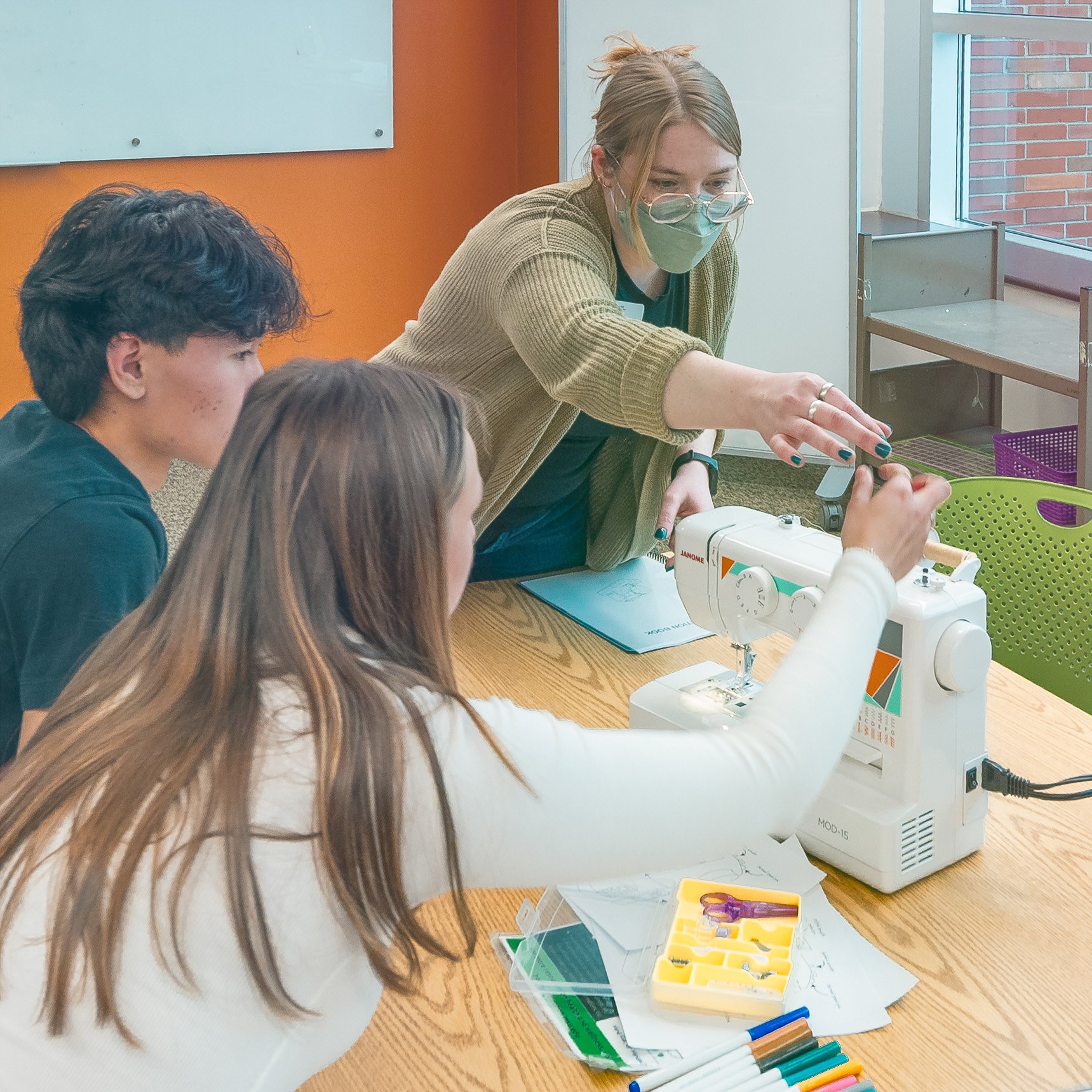 A teacher and students learning how to use a sewing machine.
