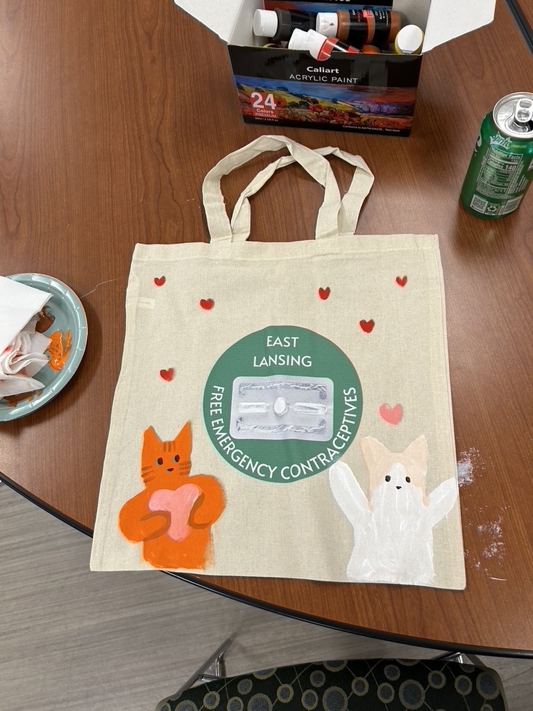 A tote bag on a table with hearts and animals painted on it, in the middle it reads