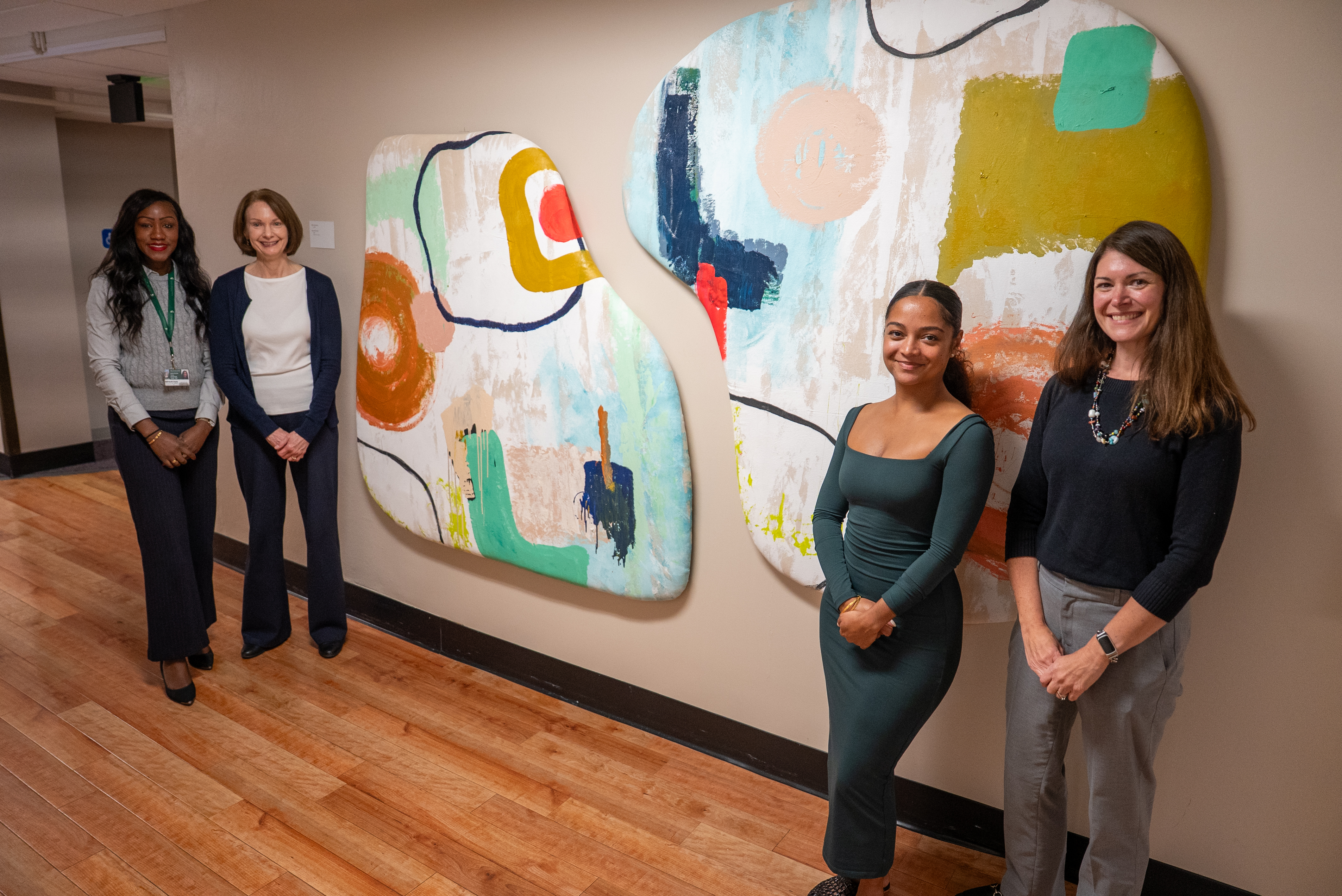 Four people including India Solomon, standing in front of India's artwork in Olin Health Center