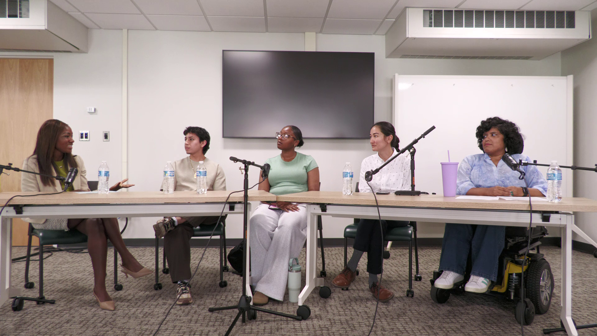 Five people sit at a table in a podcast studio. 