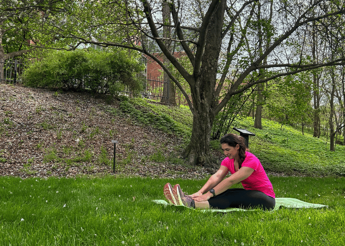 Woman stretches her legs under a tree in a botanical garden. 