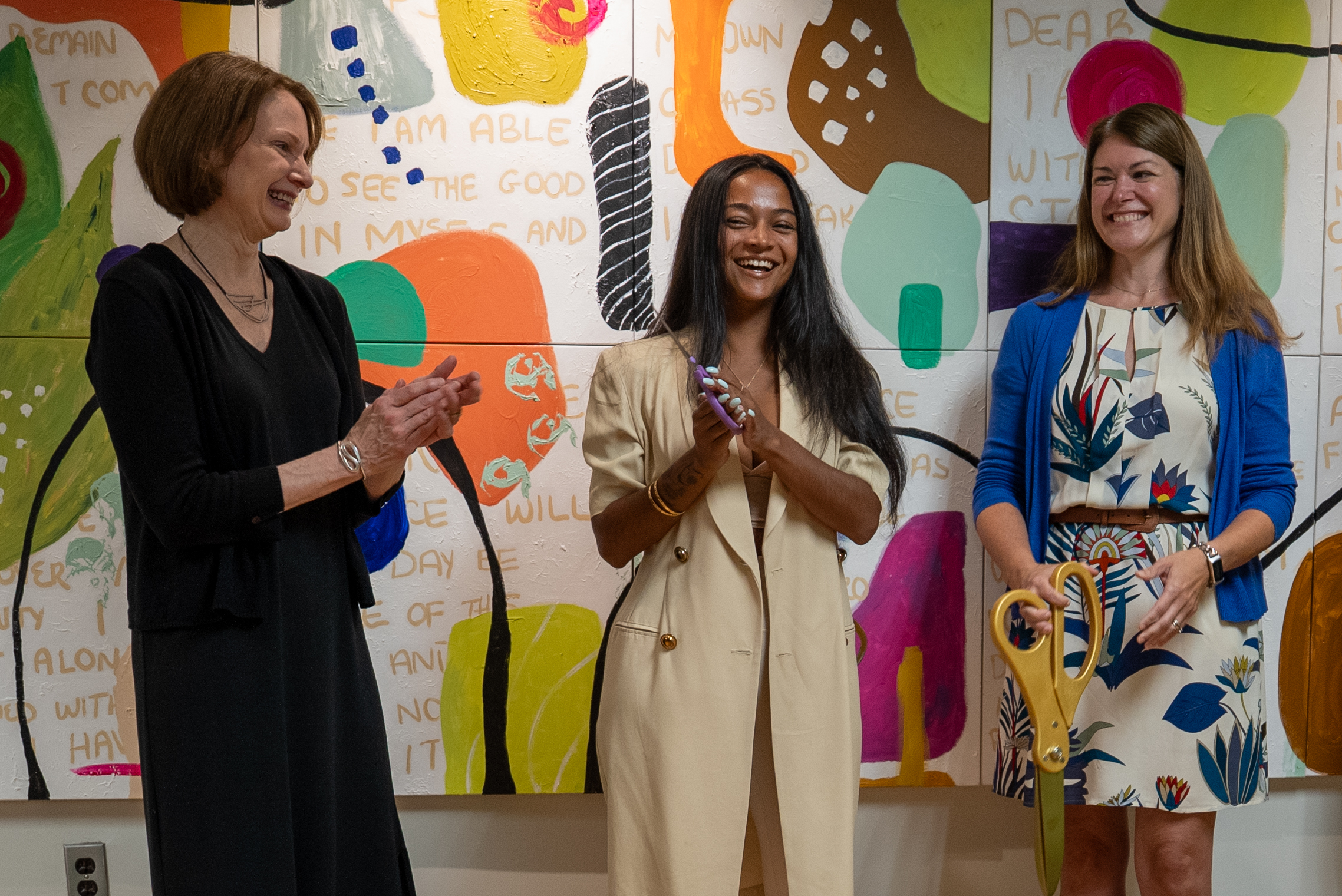 Three people standing in front of India Solomon's artwork with scissors after cutting the ribbon