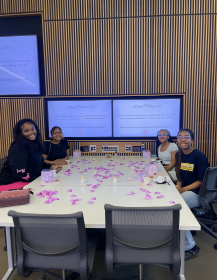 Students sitting at table with multiple big screens behind them