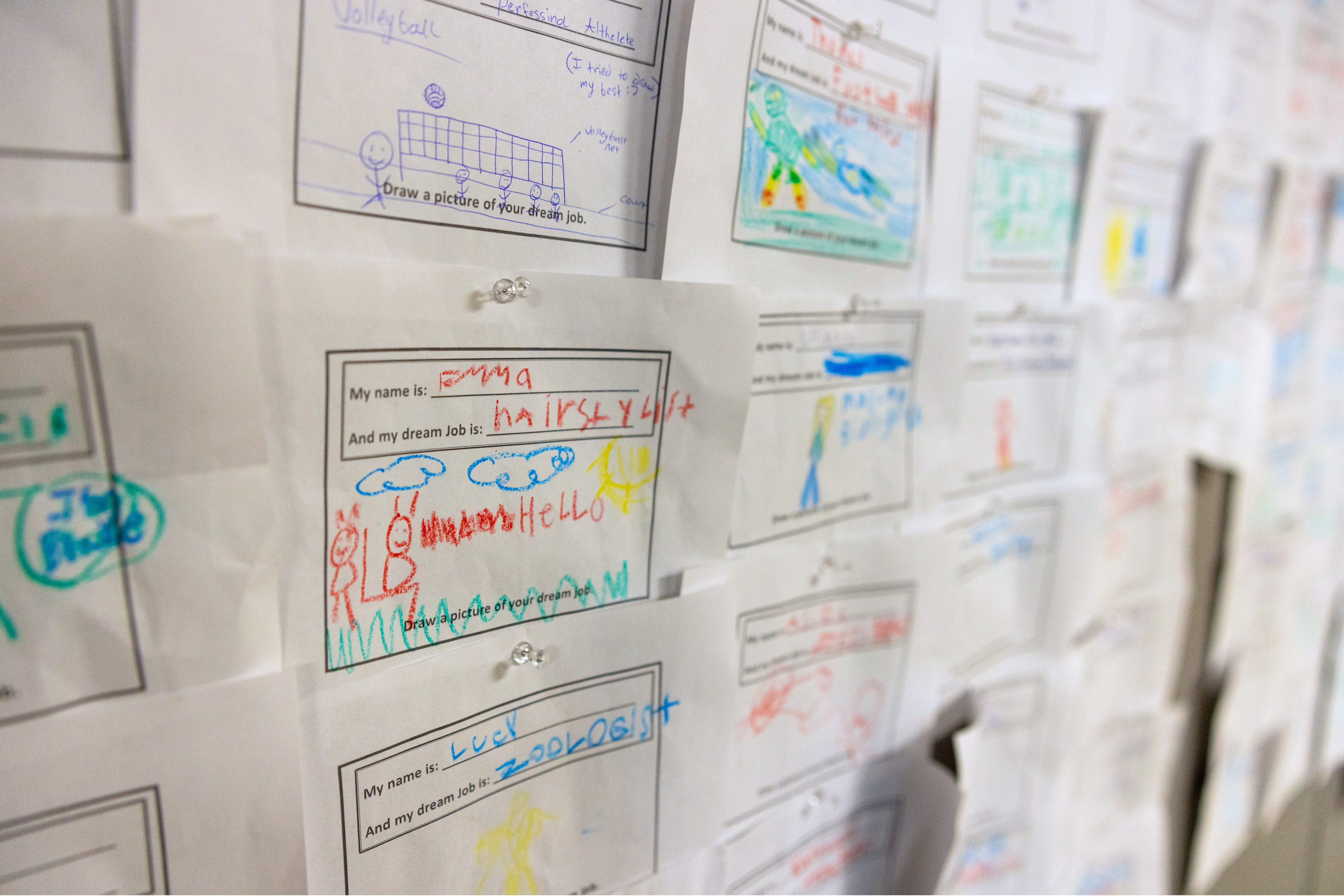 A wall display of multiple children’s drawings, each labeled with a handwritten name and dream job.