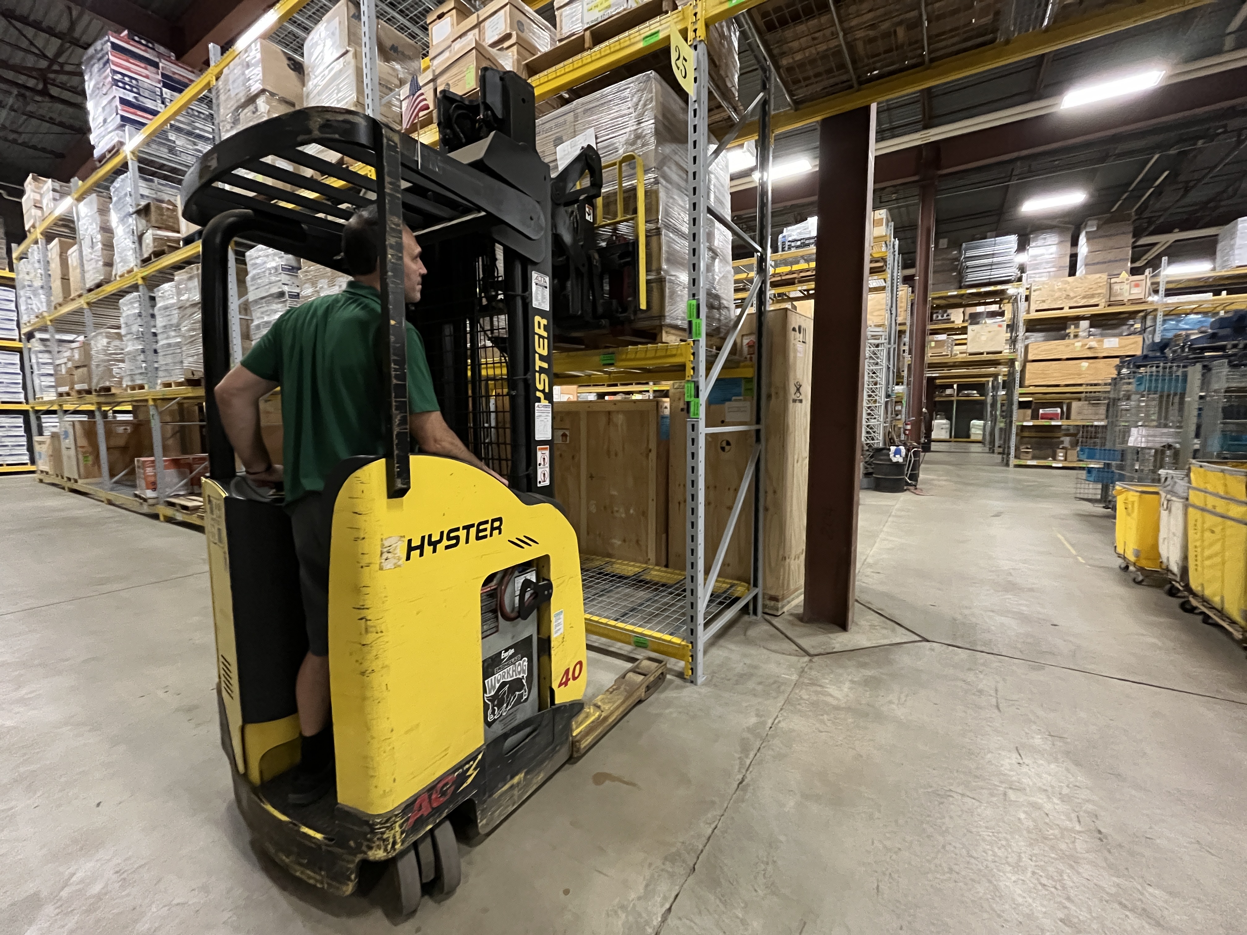 A man operating a forlift to lift a storage pallet in a warehouse