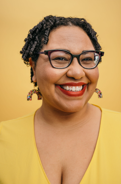 Photo of Dr. Sami Schalk a Black woman with curly hair, eyeglasses, rainbow earrings and a big smile
