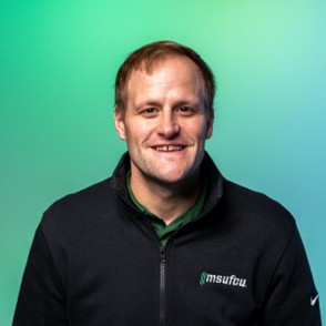 Studio-style portrait of a person wearing a dark zip-up jacket, photographed against a solid green background.