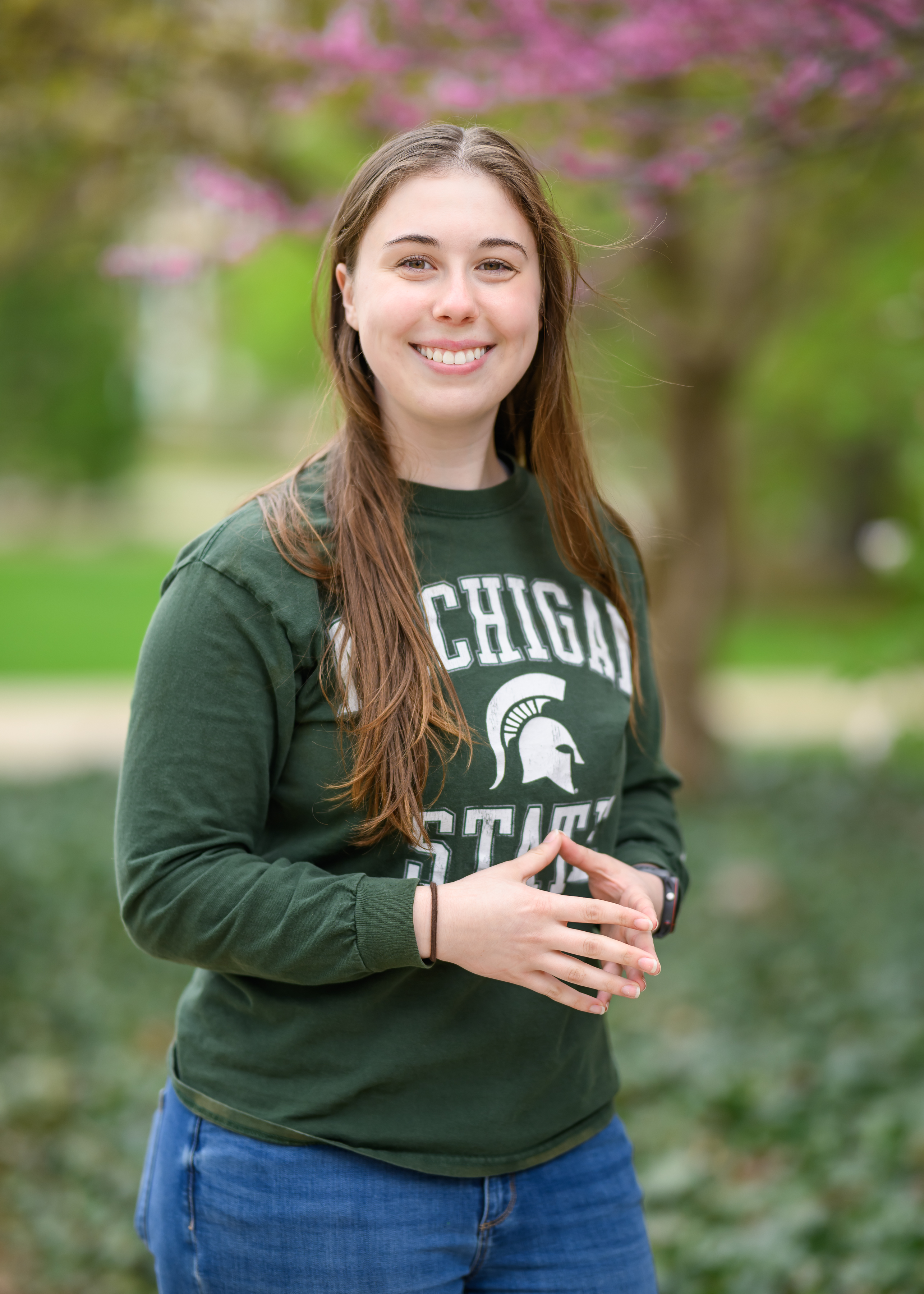 Amelie Lepley, Michigan State University 2025 Homecoming Court representative, smiling outdoors in a green MSU sweatshirt with spring blossoms in the background.