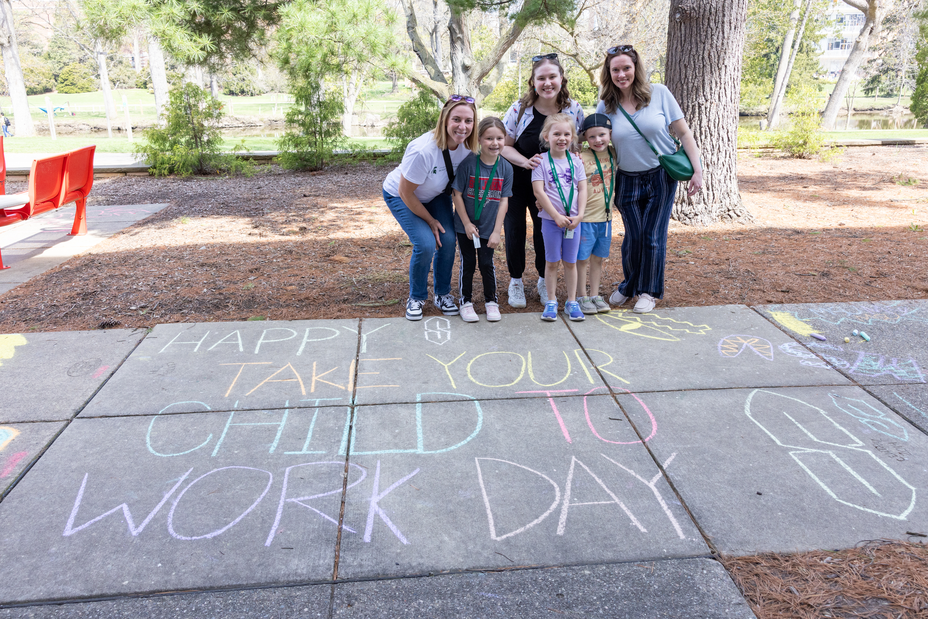 people standing behind sidewalk chalk designs that read "happy take your child to work day"