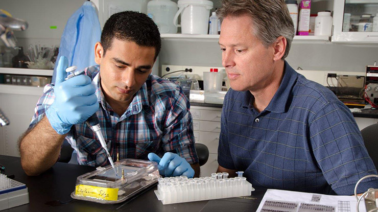 A student working on a biotechnology degree uses lab equipment with oversight from a professor who is sitting next to them.