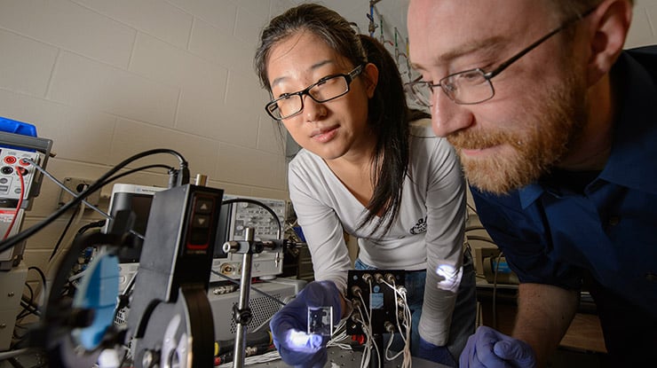 A materials science and engineering major closely examines technical equipment, with oversight from a professor.