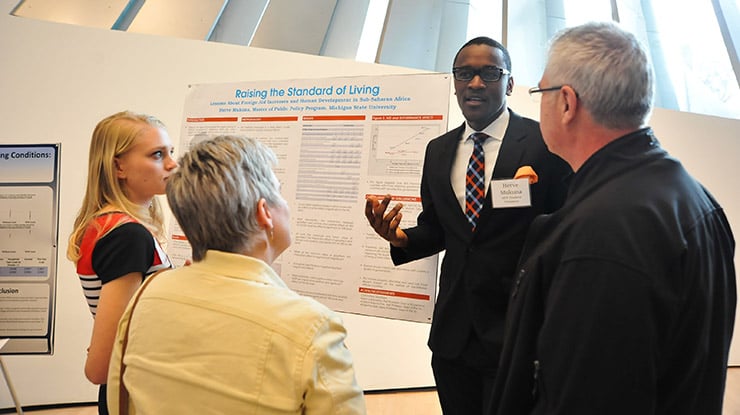 Next to a board that reads ?Raising the standard of living,? a political science major presents to a small group of people.