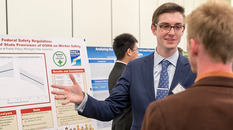 A public policy major presents information next to a board about worker safety and federal safety regulations.