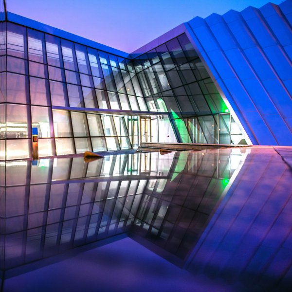 The Broad Art Museum at Michigan State University glowing with vibrant purple and blue lights against a darkening sky