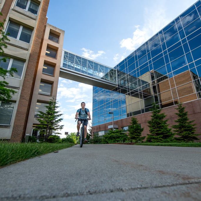 A student rides their bike under the skyway bridge between the Chemistry Building and the Biomedical and Physical Sciences Building at Michigan State University
