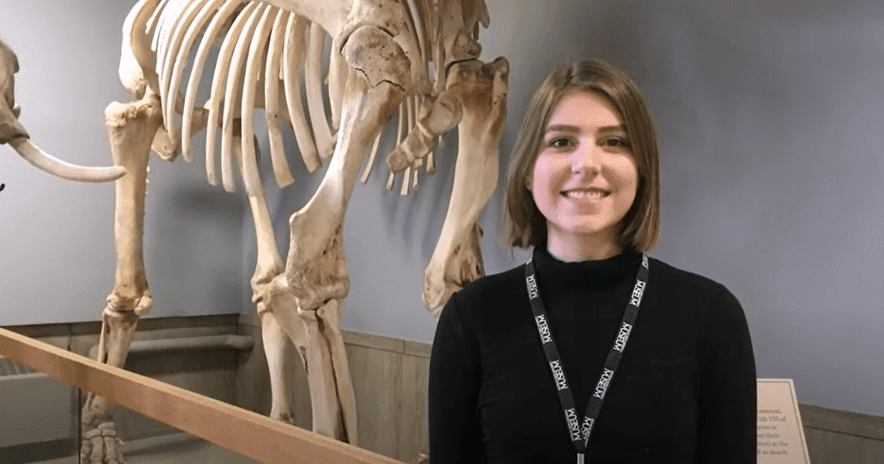 MSU student, Ally, stands in front of a reconstruction of an animal skeleton in the MSU Museum