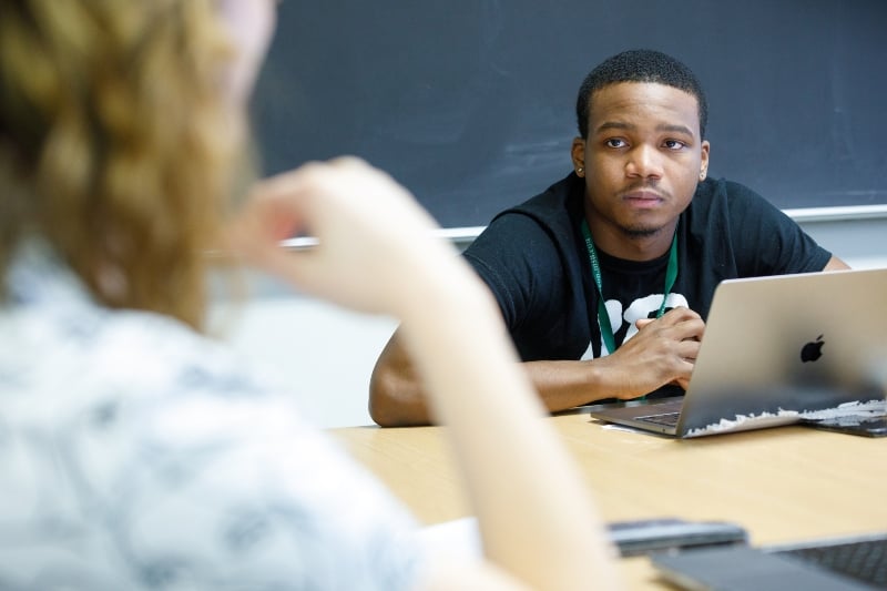 An RCAH student at MSU looks up from their laptop to listen to engage with a classmate.