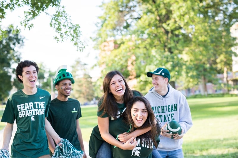 A group of Michigan State University students dressed in Spartan t-shirts walking through campus and laughing