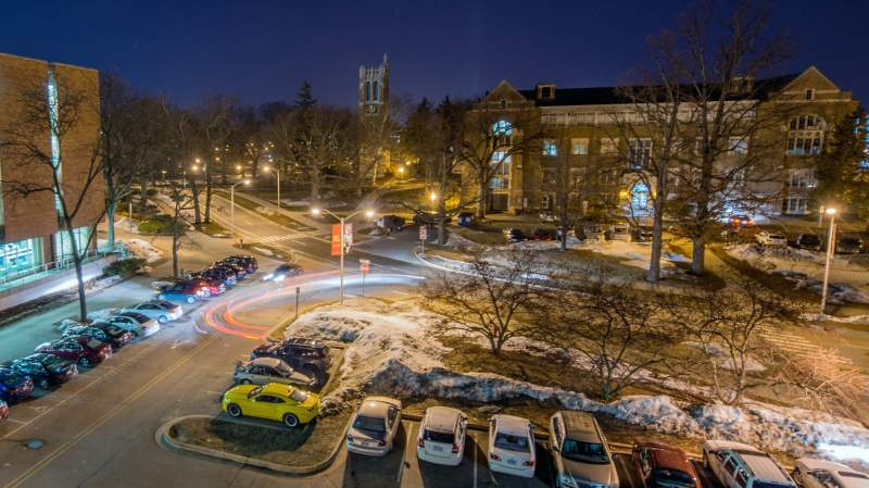An aerial time lapse of cars driving past a parking lot on MSU's campus at night