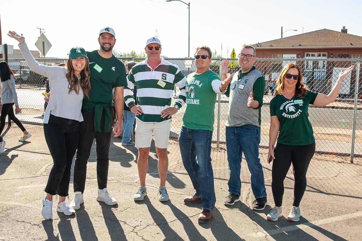 A group of AZ Spartans wearing green and white Michigan State gear, smiling and posing together outdoors while volunteering.